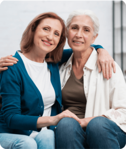 Two older women smiling and embracing, reflecting comfort and emotional support during regular respite care for carers.