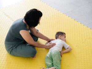 A woman supports a young boy lying on a yellow mat, showing respite care for children with autism.