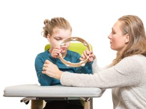 Carer assisting child with disability during tambourine therapy session to assess respite care eligibility.