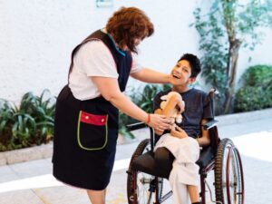 Smiling child in wheelchair playing with carer during respite care eligibility support session.