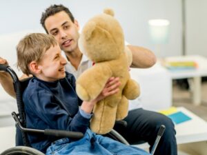 Support worker showing teddy bear to boy in wheelchair, symbolising positive respite for NDIS participants