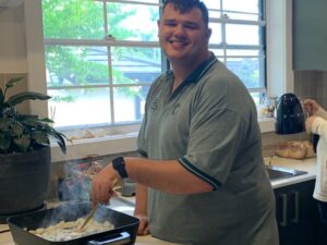 Young man with disability smiling while cooking onions in a kitchen during ndis respite in a home environment.