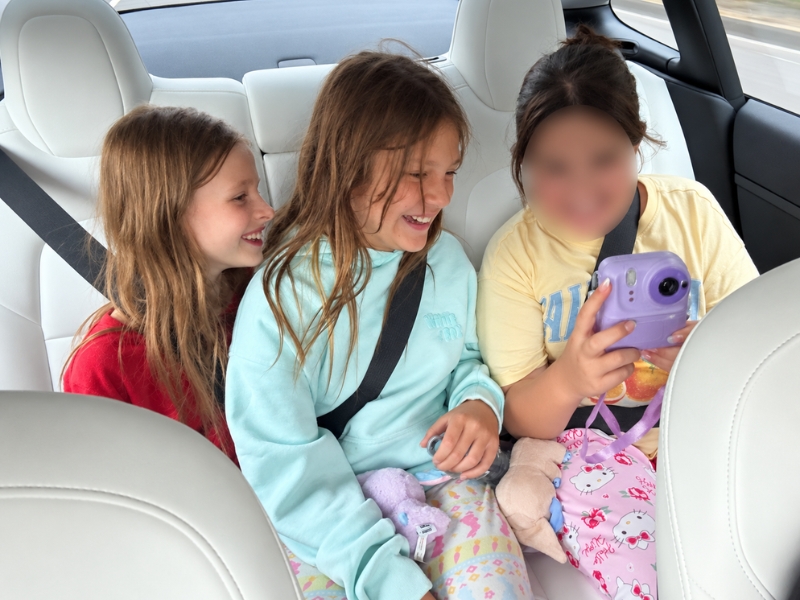 Three children looking at an instant camera in a car, accompanying an article on cultural needs during respite.