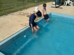 Two boys sitting at the pool edge with their legs in the water, illustrating water safety during respite.